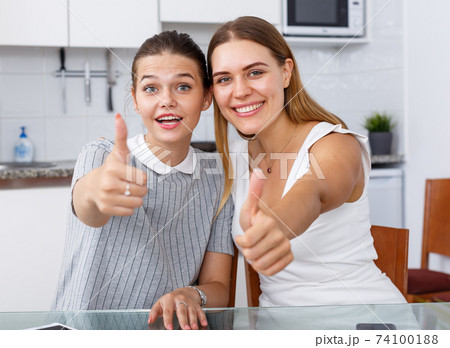 Young girlfriends sitting and holding thumbs up at kitchen table Young girlfriends sitting and holding thumbs up at kitchen table 74100188