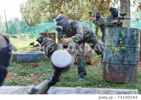 Team of adult people playing paintball on battlefield outdoor, running with guns Team of adult people playing paintball on battlefield outdoor, running with guns 74100594