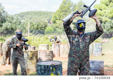 Surrendered paintball player in protective form and mask with paint splash standing with his hands up 74100638