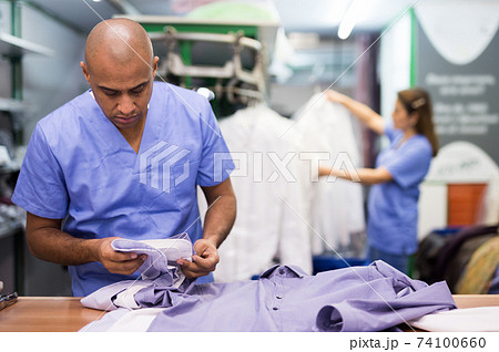 Confident man dry-cleaning worker checking clean clothes 74100660