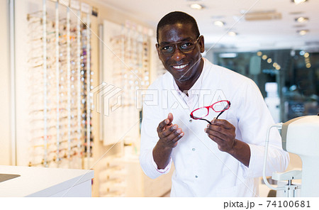 Male optician standing and offering glasses in shop 74100681