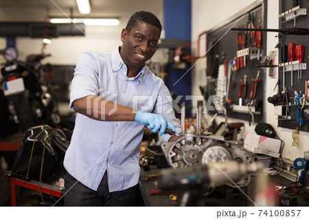 Afro american worker repairing a motorcycle engine in a garage 74100857