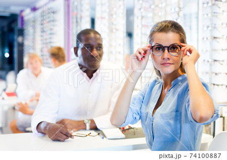 Woman trying on a spectacles in medical shop, male optician 74100887