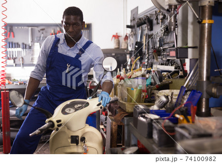 Engineer afro american man in coveralls checking motorcycle in workshop Engineer afro american man in coveralls checking motorcycle in workshop 74100982