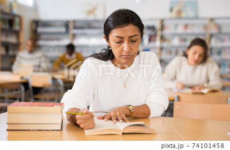 Concentrated hispanic woman reading books in public library 74101458