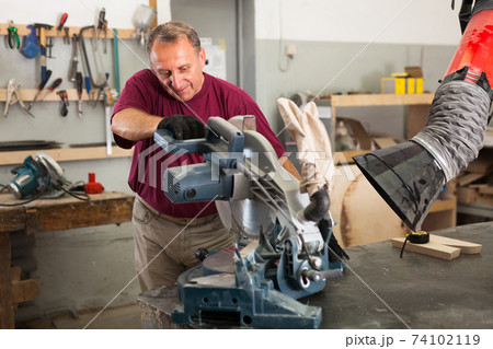 Carpenter cutting a wooden workpiece on an electical circular saw Carpenter cutting a wooden workpiece on an electical circular saw 74102119