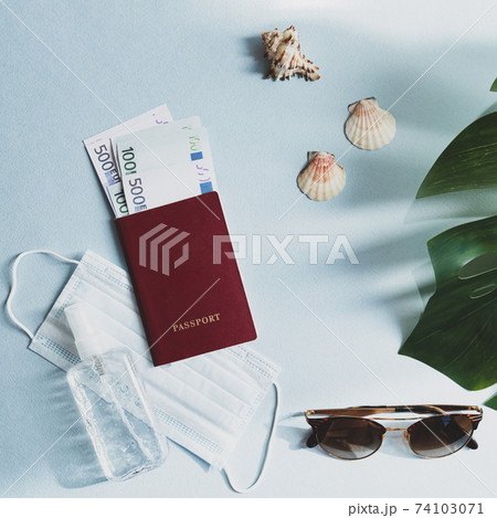 Still life scene of travel in a new reality. Passport with money, medical face mask and hand sanitizer, sunglasses, seashells and monstera palm leaf. Flat lay on a light blue table Still life scene of travel in a new reality. Passport with money, medical face mask and hand sanitizer, sunglasses, seashells and monstera palm leaf. Flat lay on a light blue table 74103071