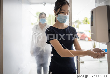 Child girl wear face mask using automatic alcohol gel dispenser,spraying on hand for disinfecting,woman in the automatic disinfection tunnel,check point for COVID-19,cleaning,safety under Coronavirus Child girl wear face mask using automatic alcohol gel dispenser,spraying on hand for disinfecting,woman in the automatic disinfection tunnel,check point for COVID-19,cleaning,safety under Coronavirus 74112641
