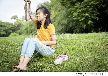 Unhappy asian female teenage is sniffing her sneakers,hold stinky shoe in hand,unpleasant smell,hot weather or after exercise,child girl with disgust,bad smell,health care,Pitted Keratolysis concept 74113118