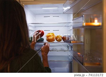 a woman's hand takes a tomato from the refrigerator shelf. The refrigerator is filled with vegetables and fruits. healthy food. healthy lifestyle concept 74113172