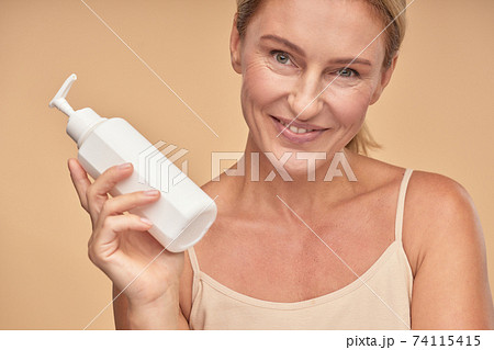 Happy beautiful adult lady showing moisturizing lotion Happy beautiful adult lady showing moisturizing lotion 74115415