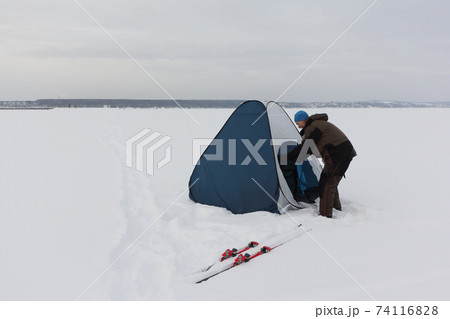 Man in suit for winter fishing putting up a tent Man in suit for winter fishing putting up a tent 74116828