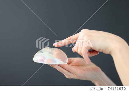 Female hand holding breast implant and pointing finger at it closeup 74121050