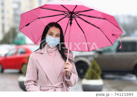 Woman in protective medical mask holding umbrella in hands Woman in protective medical mask holding umbrella in hands 74121095