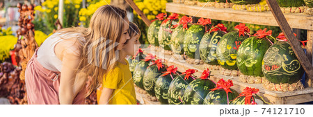 BANNER, LONG FORMAT Mom and son tourists look at Watermelons with festive engraving on Tet Eve. Tet is Lunar New Year and celebrated during four days in Vietnam TEXT TRANSLATION from Vietnamese BANNER, LONG FORMAT Mom and son tourists look at Watermelons with festive engraving on Tet Eve. Tet is Lunar New Year and celebrated during four days in Vietnam TEXT TRANSLATION from Vietnamese 74121710