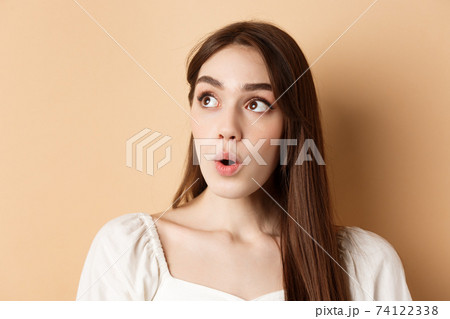 Close up portrait of excited pretty woman looking aside logo, say wow with amazed face, standing on beige background Close up portrait of excited pretty woman looking aside logo, say wow with amazed face, standing on beige background 74122338