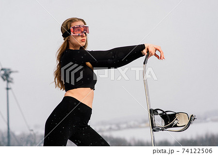 Happy girl snowboarder posing in sunglasses with snowboard Happy girl snowboarder posing in sunglasses with snowboard 74122506