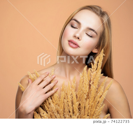 Calm Blonde girl with a bunch spring dry field flowers near the face - over colored background. Beauty face care concept. Calm Blonde girl with a bunch spring dry field flowers near the face - over colored background. Beauty face care concept. 74122735