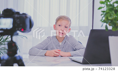 Child blogger videotapes his vlog at home. Boy recording his video blog. White boy speaks in front of a video camera for his blog channel. Little 8 year vlogger makes online streaming using smartphone Child blogger videotapes his vlog at home. Boy recording his video blog. White boy speaks in front of a video camera for his blog channel. Little 8 year vlogger makes online streaming using smartphone 74123328