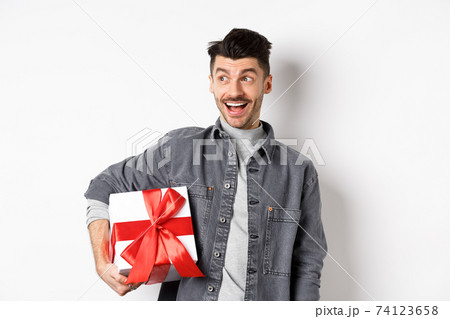 Cheerful handsome guy looking at empty space with amazed smile, checking out special valentines day offer, holding big romantic gift box, standing on white background Cheerful handsome guy looking at empty space with amazed smile, checking out special valentines day offer, holding big romantic gift box, standing on white background 74123658