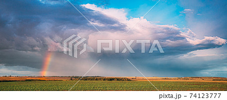 Dramatic Sky During Rain With Rainbow On Horizon Above Rural Landscape Field. Agricultural And Weather Forecast Concept. Countryside Meadow In Rainy Day Dramatic Sky During Rain With Rainbow On Horizon Above Rural Landscape Field. Agricultural And Weather Forecast Concept. Countryside Meadow In Rainy Day 74123777