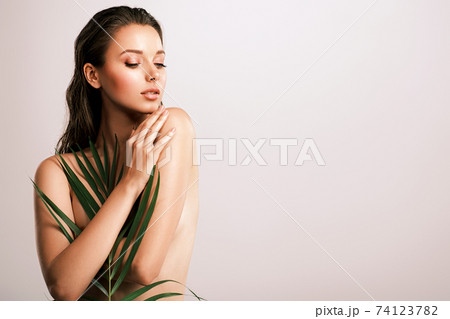 White woman with healthy skin of body and palm leaves. Tanned body of an attractive girl with green plants. Large palm leaves cover the body. White woman with healthy skin of body and palm leaves. Tanned body of an attractive girl with green plants. Large palm leaves cover the body. 74123782