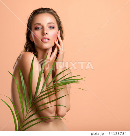 White woman with healthy skin of body and palm leaves. Tanned body of an attractive girl with green plants. Large palm leaves cover the body. White woman with healthy skin of body and palm leaves. Tanned body of an attractive girl with green plants. Large palm leaves cover the body. 74123784