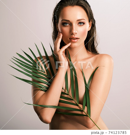 White woman with healthy skin of body and palm leaves. Tanned body of an attractive girl with green plants. Large palm leaves cover the body. White woman with healthy skin of body and palm leaves. Tanned body of an attractive girl with green plants. Large palm leaves cover the body. 74123785