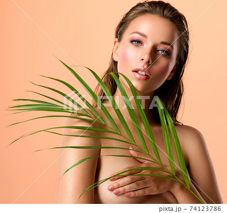 White woman with healthy skin of body and palm leaves. Tanned body of an attractive girl with green plants. Large palm leaves cover the breast. White woman with healthy skin of body and palm leaves. Tanned body of an attractive girl with green plants. Large palm leaves cover the breast. 74123786