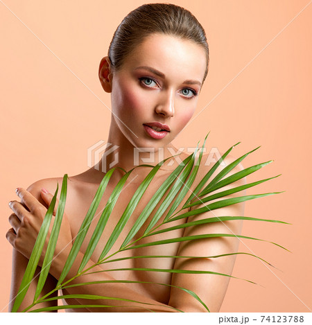 White woman with healthy skin of body and palm leaves. Tanned body of an attractive girl with green plants. Large palm leaves cover the breast. White woman with healthy skin of body and palm leaves. Tanned body of an attractive girl with green plants. Large palm leaves cover the breast. 74123788
