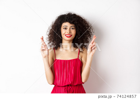 Hopeful beauty girl with curly hair, cross fingers for good luck and smiling, making wish or praying, standing on white background 74124857