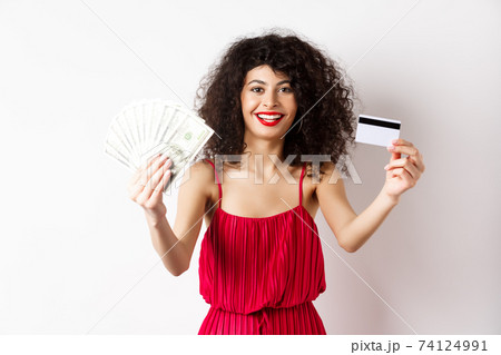 Shopping. Lucky woman in elegant dress, showing money and plastic credit card, smiling pleased, wearing makeup, white background Shopping. Lucky woman in elegant dress, showing money and plastic credit card, smiling pleased, wearing makeup, white background 74124991