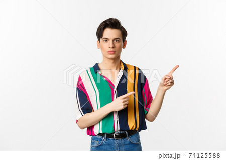 Portrait of young handsome man pointing fingers at upper right corner, showing logo, standing over white background 74125588