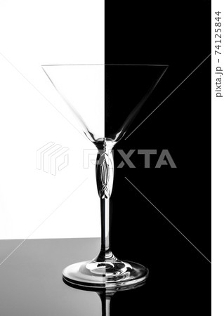 Empty transparent martini glass on mirrored surface over black and white background, studio advertising shot, copy space 74125844
