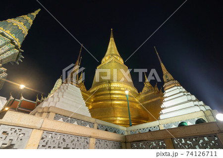 Golden pagoda at Temple of the Emerald Buddha in Bangkok, Thailand. Wat Phra Kaew and Grand palace in old town, urban city. Buddhist temple, Thai architecture. A tourist attraction at night. 74126711