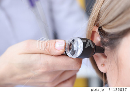 Otorhinolaryngologist looking at patients ear using an otoscope closeup Otorhinolaryngologist looking at patients ear using an otoscope closeup 74126857