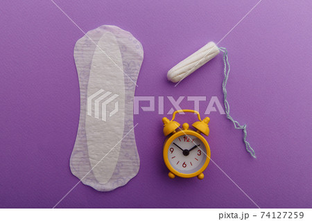 Female's menstrual cycle concept. Sanitary pad with yellow alarm clock and tampon 74127259