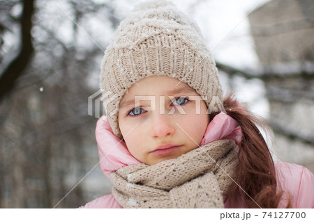 Sad child girl in warm knitted winter clothes spent time outdoors and got frozen. 74127700