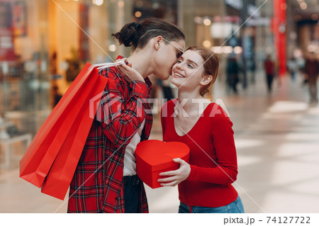 A guy gives his girlfriend a heart-shaped box from shopping bag in Valentine's Day. Young couple kissing in shopping mall. 74127722