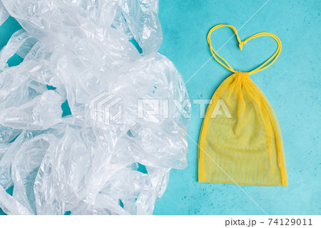 Mesh reusable yellow bag in form of heart vs a lot of plastic bags. Eco concept. Zero waste shopping 74129011