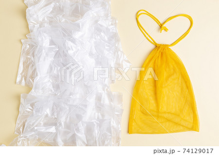 Mesh reusable yellow bag in form of heart vs a lot of plastic bags. Eco concept. Zero waste shopping 74129017