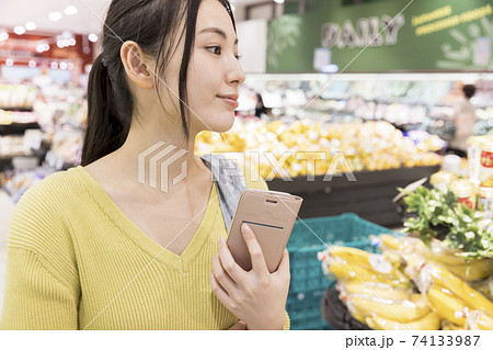 スーパーでスマホをチェックする女性買い物客 74133987