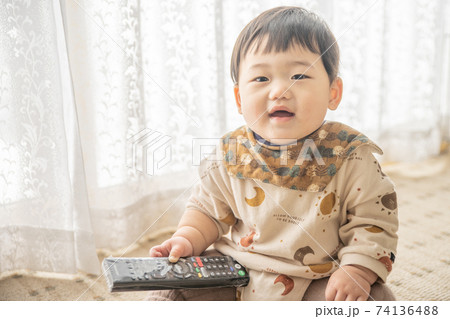 窓辺でお座りをしてリモコンで遊んでいる赤ちゃん 窓辺でお座りをしてリモコンで遊んでいる赤ちゃん 74136488
