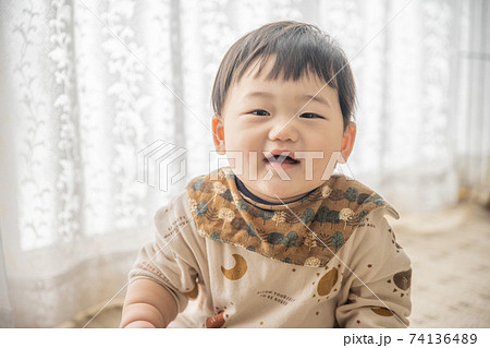 窓辺でお座りをしてリモコンで遊んでいる赤ちゃん 窓辺でお座りをしてリモコンで遊んでいる赤ちゃん 74136489