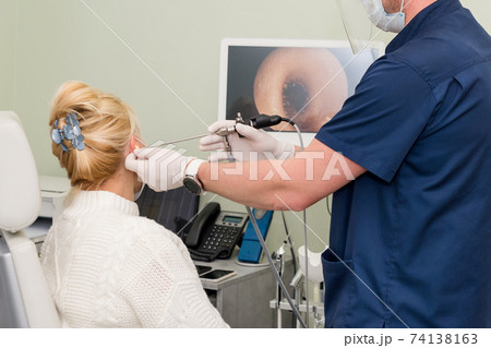 ENT doctor with tools wearing mask and gloves examines the patient's ear. Otolaryngologist doing otitus examination, video otoscopy procedure. Hearing clinic ENT doctor with tools wearing mask and gloves examines the patient's ear. Otolaryngologist doing otitus examination, video otoscopy procedure. Hearing clinic 74138163