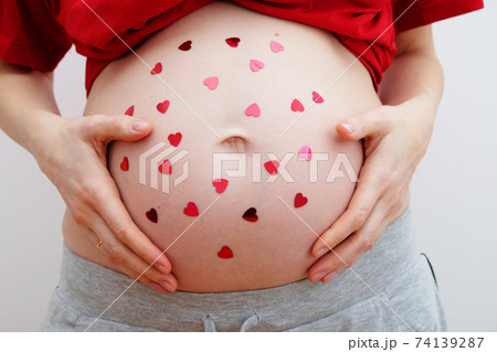 Happy Valentines day. A pregnant woman with heart-shaped sequins on her tummy. 74139287