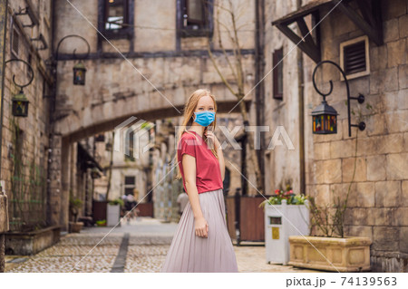 Young woman tourist wearing a medical mask during COVID-19 coronavirus walks down the street in a European city after the end of COVID-19 coronavirus. quarantine is over 74139563