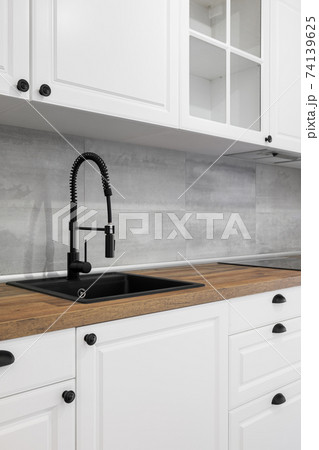 Simple and elegant kitchen with wooden countertop, white cupboards, drawers and black sink. 74139625
