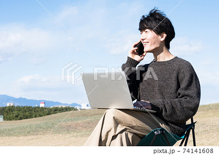 屋外でパソコンを見ながら通話する男性 74141608