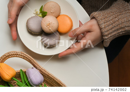 Female hands holding a plate of French Colorful Macarons to place on coffee table with tulips 74142002